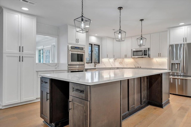 kitchen with appliances with stainless steel finishes, pendant lighting, white cabinetry, a center island, and light wood-type flooring