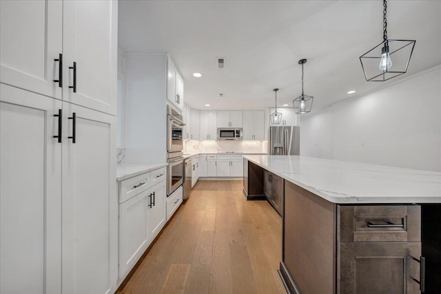 kitchen with a spacious island, white cabinetry, light stone counters, pendant lighting, and stainless steel appliances