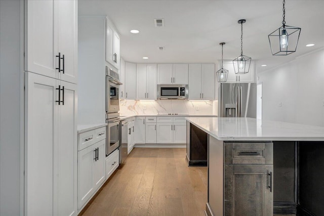 kitchen featuring decorative light fixtures, white cabinets, a center island, stainless steel appliances, and light stone countertops