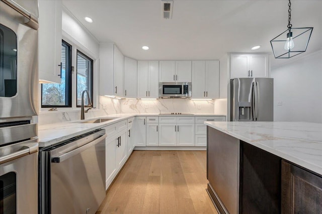 kitchen with sink, white cabinetry, light stone counters, decorative light fixtures, and appliances with stainless steel finishes