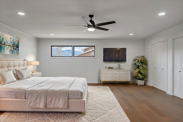 bedroom with crown molding, wood-type flooring, ceiling fan, and two closets