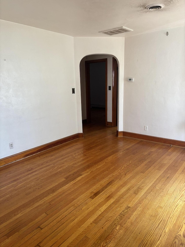 unfurnished room featuring light wood-style flooring, visible vents, and arched walkways