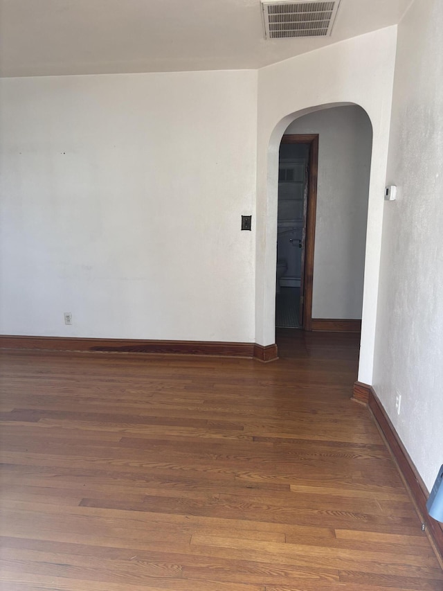 unfurnished room with wood finished floors, arched walkways, visible vents, and baseboards