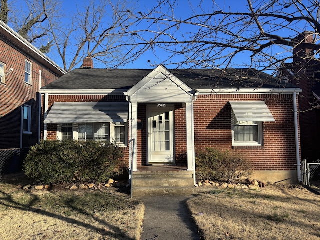 bungalow-style house with brick siding, a chimney, and roof with shingles