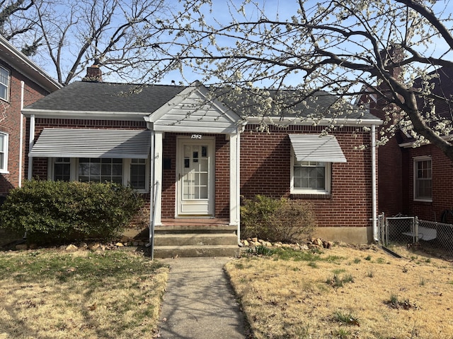 bungalow featuring fence, brick siding, roof with shingles, and a chimney