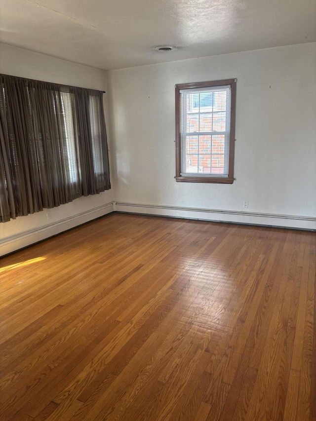 empty room with baseboard heating, visible vents, and wood finished floors