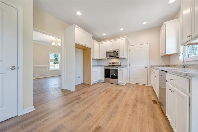 kitchen with light wood-type flooring, light stone counters, stainless steel appliances, an inviting chandelier, and white cabinets