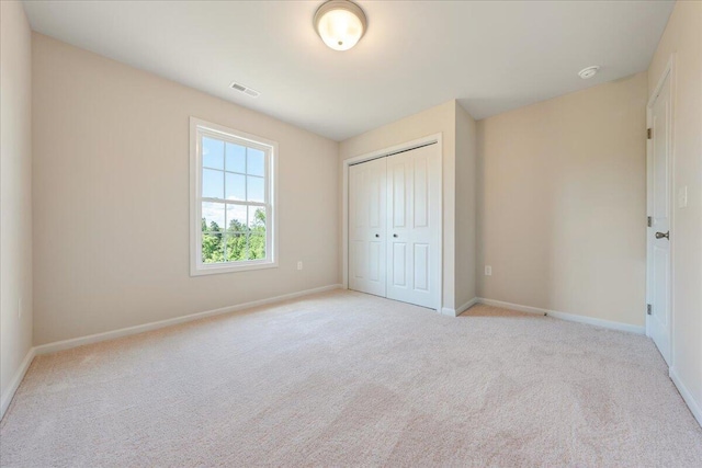 unfurnished bedroom with light colored carpet and a closet