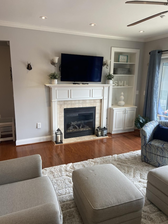 living room featuring built in shelves, hardwood / wood-style flooring, crown molding, and a tiled fireplace