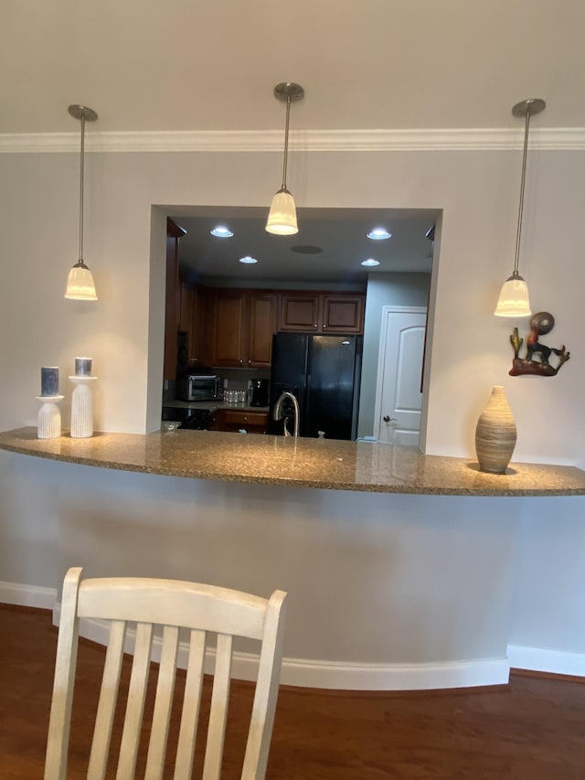 kitchen with pendant lighting, light stone counters, ornamental molding, and black refrigerator with ice dispenser