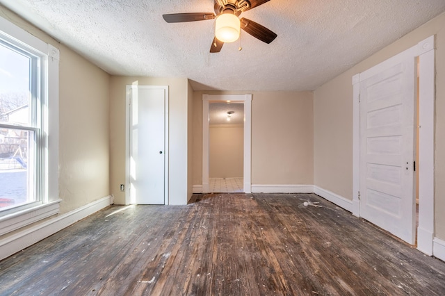 spare room with a textured ceiling, dark wood-type flooring, a wealth of natural light, and ceiling fan