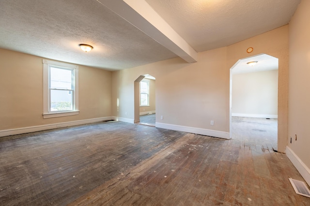 empty room with a textured ceiling, a wealth of natural light, and dark hardwood / wood-style floors