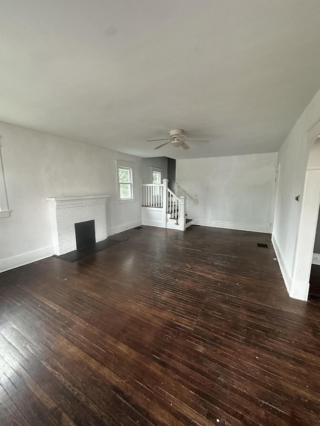 unfurnished living room with a fireplace, ceiling fan, and dark wood-type flooring