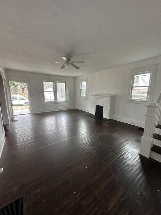 unfurnished living room featuring ceiling fan, dark hardwood / wood-style floors, plenty of natural light, and a brick fireplace