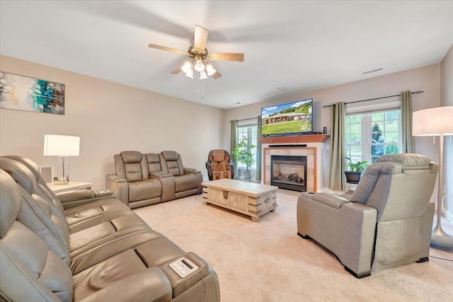 living room with ceiling fan, a tile fireplace, and light carpet