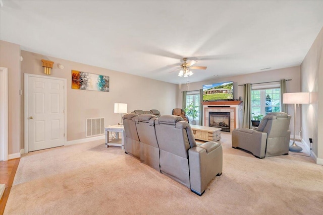 carpeted living room with a tiled fireplace, ceiling fan, and plenty of natural light