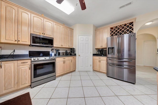 kitchen featuring appliances with stainless steel finishes, light tile patterned floors, ceiling fan, light brown cabinetry, and tasteful backsplash