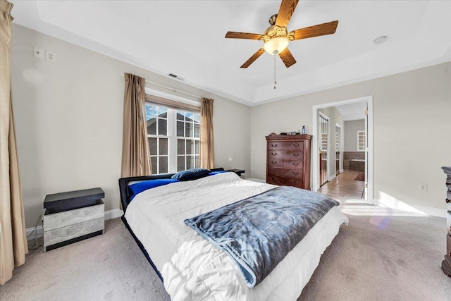 carpeted bedroom with ensuite bathroom, a raised ceiling, and ceiling fan