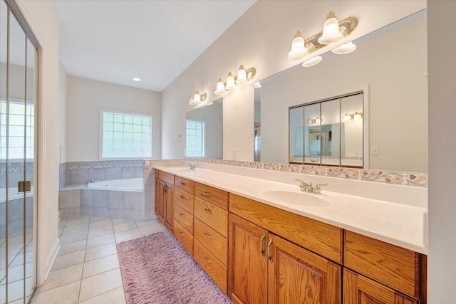 bathroom with a relaxing tiled tub, vanity, and tile patterned floors