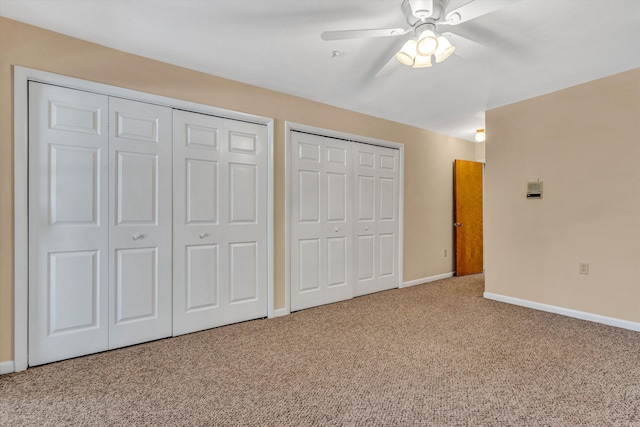 unfurnished bedroom featuring carpet flooring, ceiling fan, and multiple closets