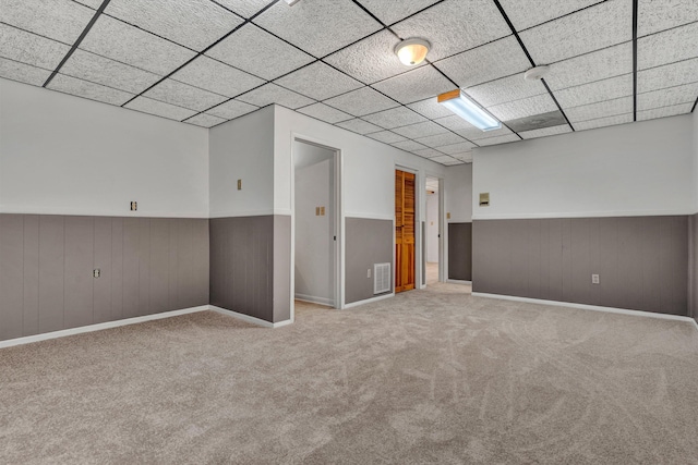 basement featuring light carpet, a drop ceiling, and wood walls