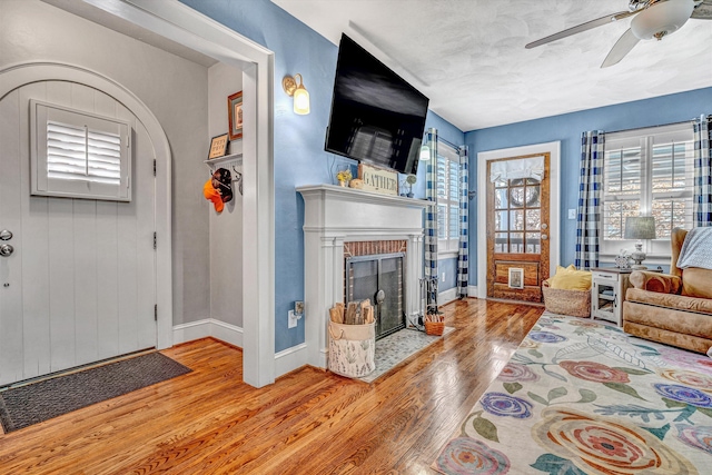 living room with a brick fireplace, light hardwood / wood-style flooring, and ceiling fan