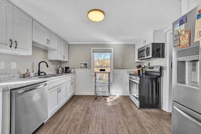 kitchen with sink, white cabinets, light hardwood / wood-style floors, crown molding, and appliances with stainless steel finishes