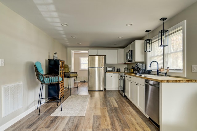 kitchen featuring wood counters, appliances with stainless steel finishes, white cabinetry, and pendant lighting