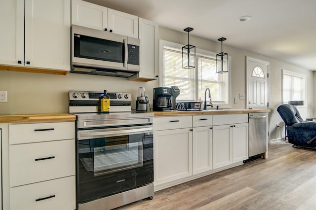 kitchen with a wealth of natural light, wooden counters, pendant lighting, white cabinets, and appliances with stainless steel finishes