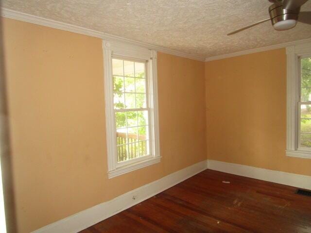 empty room featuring plenty of natural light, dark hardwood / wood-style floors, and ornamental molding