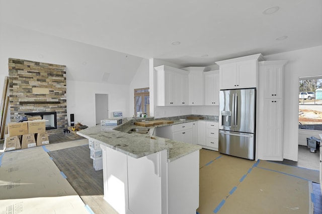 kitchen with stainless steel refrigerator with ice dispenser, a breakfast bar area, white cabinetry, kitchen peninsula, and a fireplace