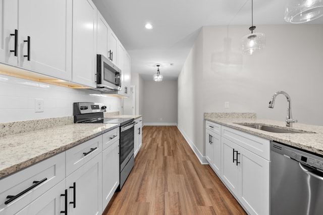 kitchen with pendant lighting, stainless steel appliances, white cabinetry, and light stone counters