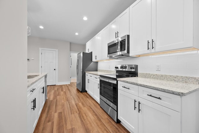 kitchen featuring light stone countertops, stainless steel appliances, white cabinetry, and light hardwood / wood-style flooring