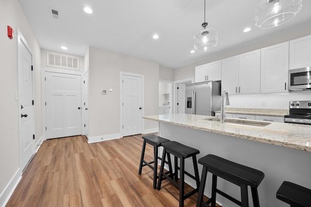 kitchen featuring sink, light stone counters, light hardwood / wood-style flooring, white cabinets, and appliances with stainless steel finishes