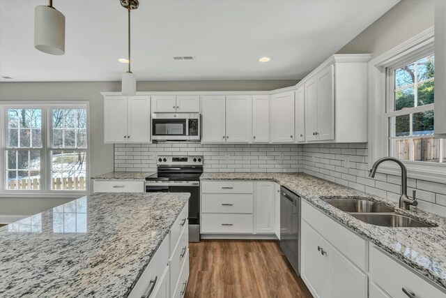 kitchen with decorative light fixtures, stainless steel appliances, a kitchen island, white cabinets, and sink