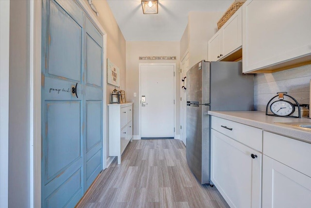 kitchen featuring light wood-type flooring, decorative backsplash, white cabinets, and stainless steel refrigerator