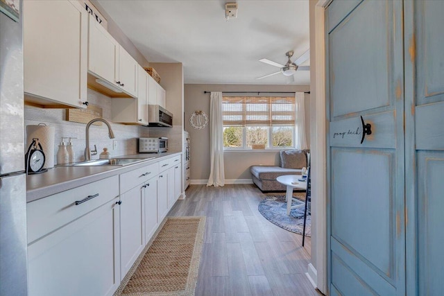 kitchen featuring ceiling fan, backsplash, sink, white cabinetry, and light hardwood / wood-style flooring