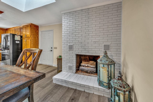 kitchen featuring crown molding, a skylight, stainless steel refrigerator, and light wood-type flooring