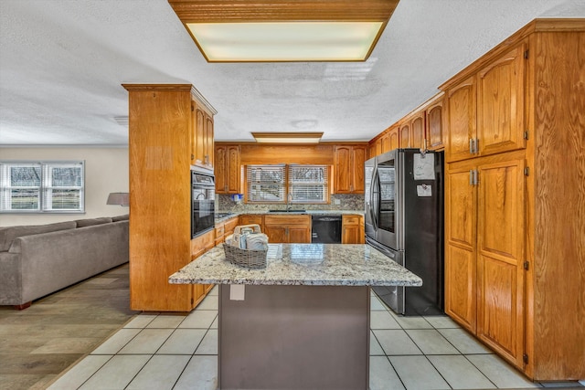 kitchen with light stone countertops, a wealth of natural light, black appliances, and a kitchen island