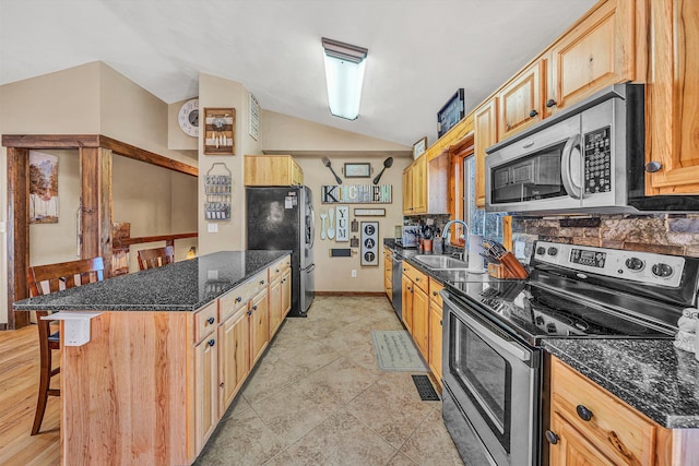 kitchen featuring stainless steel appliances, a kitchen breakfast bar, light brown cabinetry, vaulted ceiling, and sink