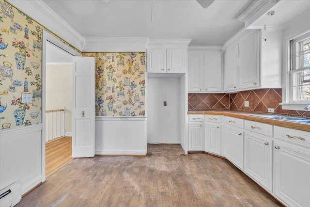 kitchen with sink, a baseboard radiator, white cabinetry, and ornamental molding