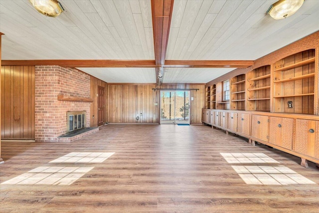 unfurnished living room with hardwood / wood-style floors, built in shelves, a fireplace, wood walls, and beam ceiling