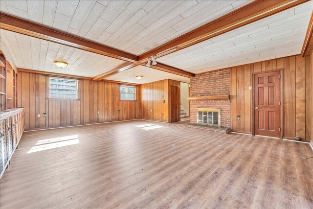 unfurnished living room featuring a brick fireplace, wood ceiling, beamed ceiling, and wooden walls