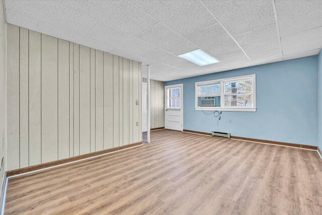 basement featuring wood walls, light hardwood / wood-style floors, and a paneled ceiling