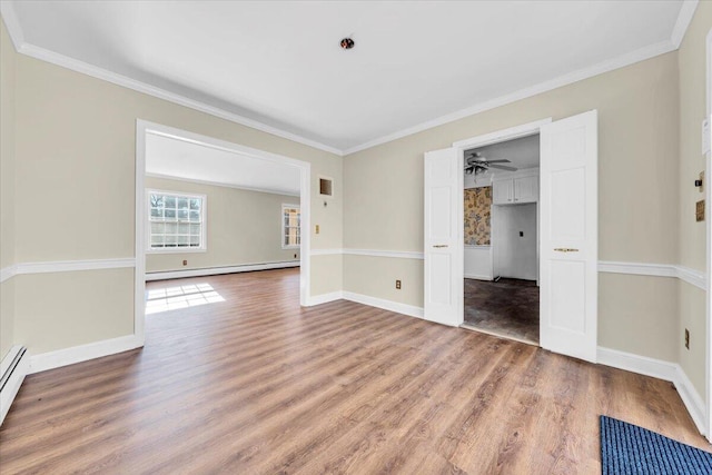 empty room with baseboard heating, wood-type flooring, and crown molding