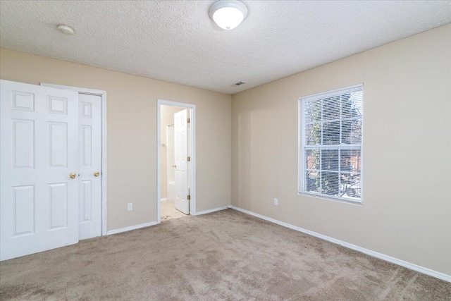 unfurnished bedroom featuring multiple windows, a textured ceiling, light carpet, and connected bathroom