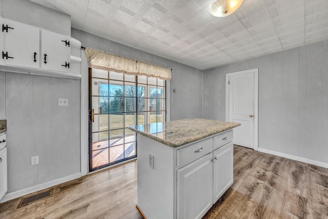 kitchen with white cabinetry, a center island, light wood-type flooring, and light stone countertops