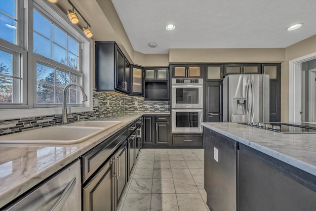 kitchen featuring appliances with stainless steel finishes, backsplash, light stone counters, and sink