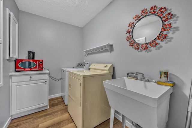 laundry area with a textured ceiling, wood-type flooring, washing machine and dryer, cabinets, and sink