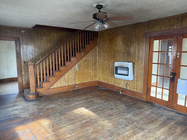 unfurnished living room featuring heating unit, wood walls, ceiling fan, dark hardwood / wood-style floors, and a textured ceiling